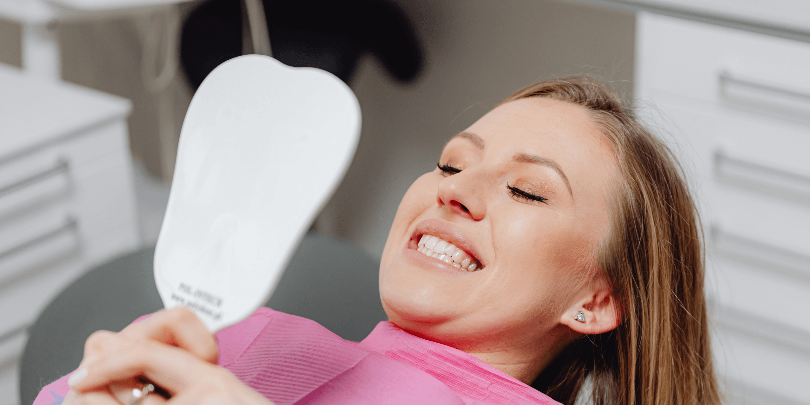Woman smiling, looking in a mirror at her teeth after they have been whitened