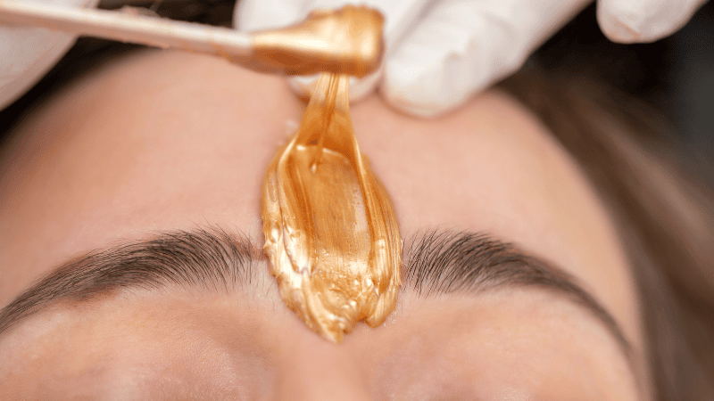 Close up image of woman getting her forehead waxed with woman with white gloves on