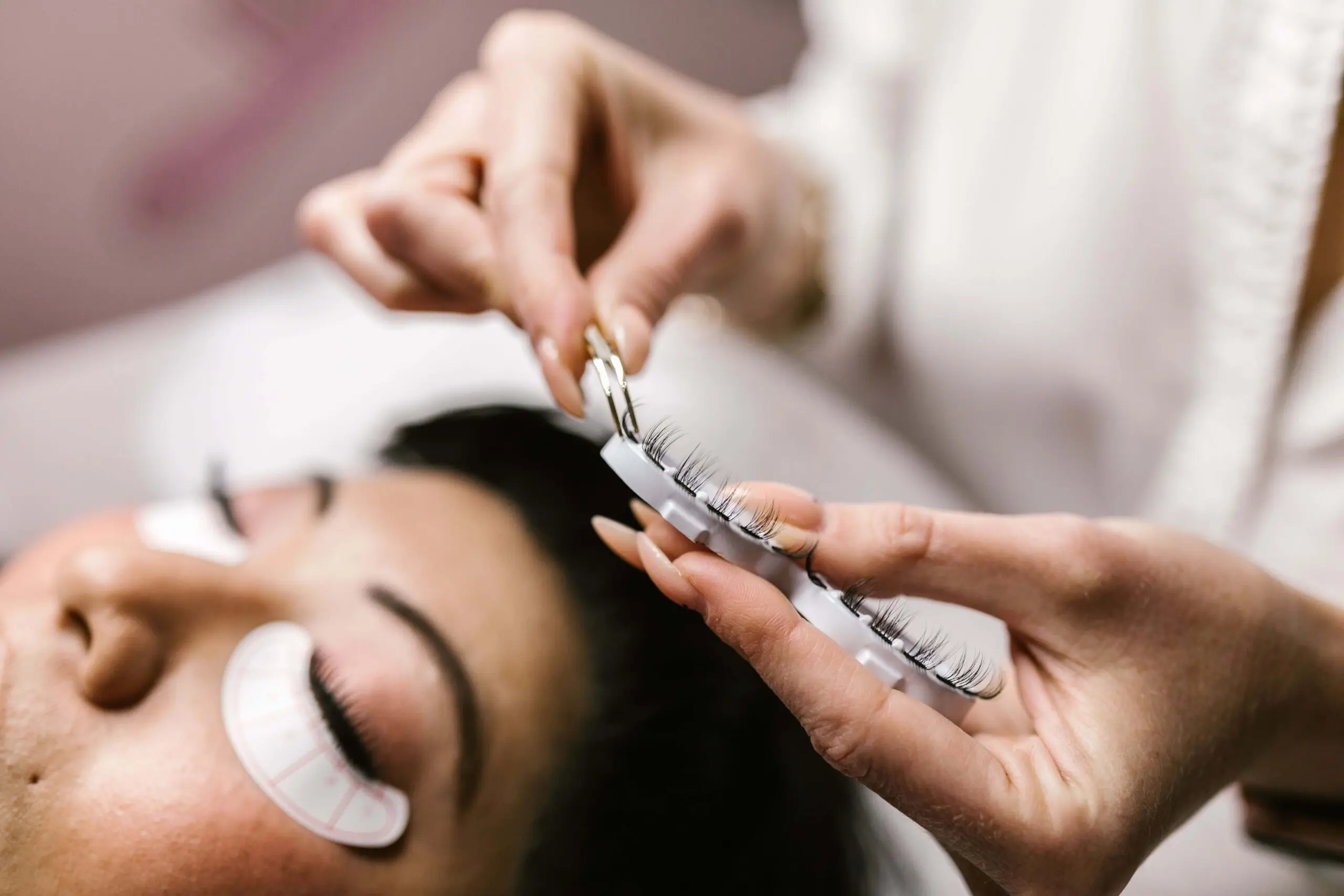 Beauty header image Woman applying lash extensions to client laying down in the chair