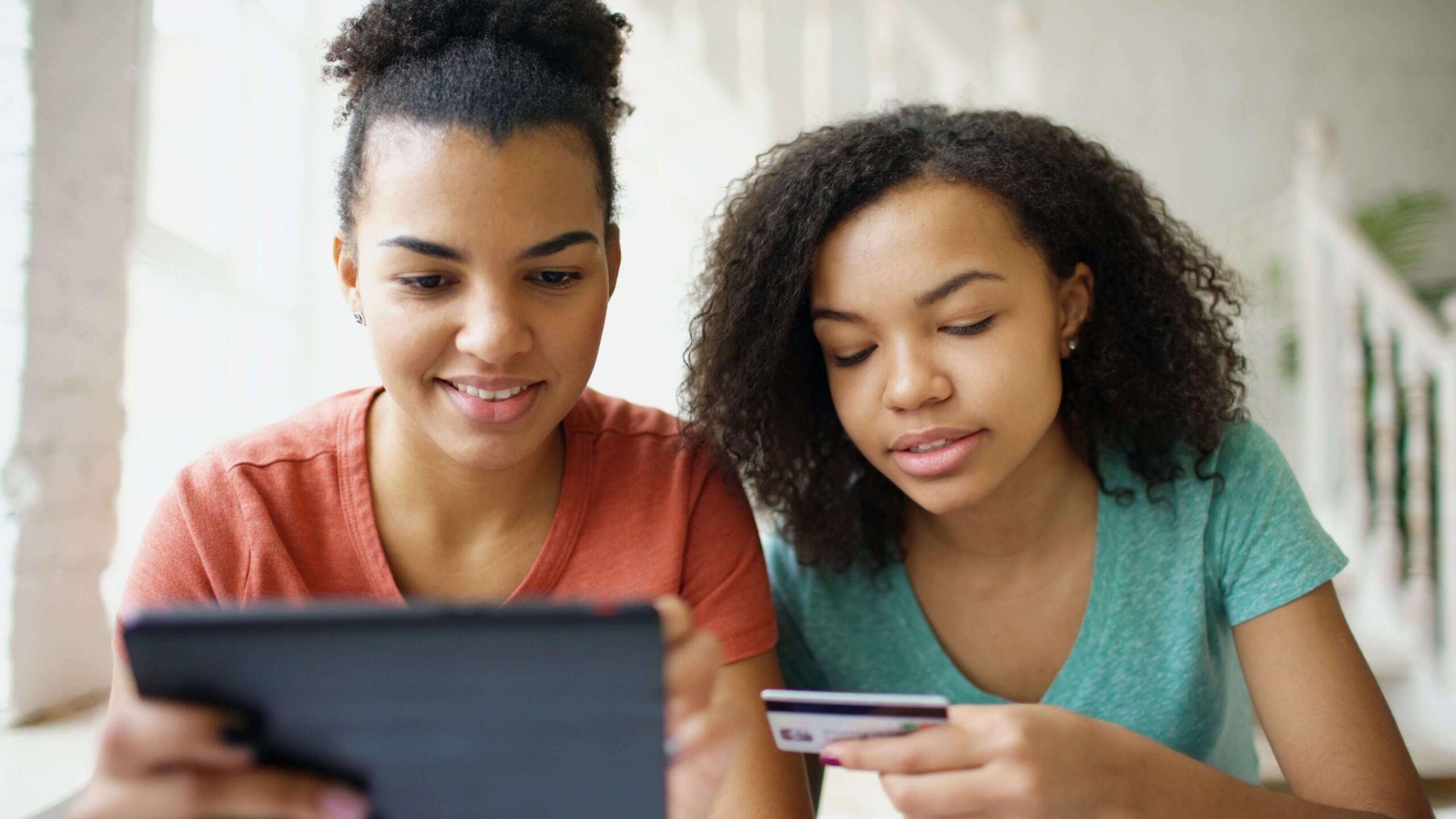 Two women looking at a tablet while holding a bank card to pay online